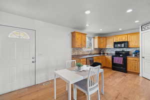 Kitchen featuring black appliances, light wood-style floors, tasteful backsplash, recessed lighting, and dark stone counters