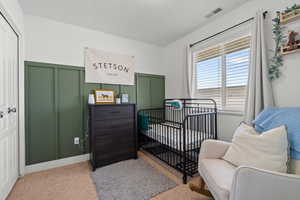 Bedroom featuring a nursery area, a decorative wall, and wainscoting