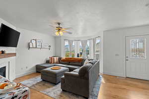 Living room with light wood-style floors, a textured ceiling, ceiling fan, and a glass covered fireplace