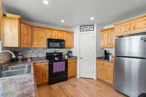 Kitchen featuring black appliances, backsplash, light wood-style flooring, recessed lighting, and dark countertops