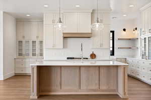 Kitchen featuring glass insert cabinets, open shelves, a kitchen island with sink, light stone countertops, and light wood-style floors