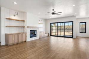 Unfurnished living room with light wood-style flooring, a textured ceiling, ceiling fan, a tiled fireplace, and recessed lighting