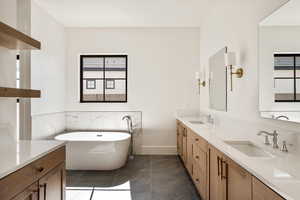 Full bathroom with a soaking tub, double vanity, and dark tile patterned floors