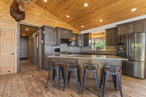 Kitchen with vaulted ceiling, stainless steel appliances, a breakfast bar, wood ceiling, and dark brown cabinetry