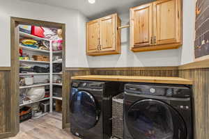 Laundry area featuring wood finished floors, cabinet space, a wainscoted wall, washing machine and clothes dryer, and recessed lighting