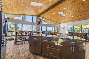 Kitchen with dark brown cabinets, dark stone counters, stainless steel refrigerator with ice dispenser, light wood-style flooring, and high vaulted ceiling