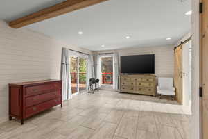 Living area featuring wood walls, a barn door, recessed lighting, beamed ceiling, and wood finish floors