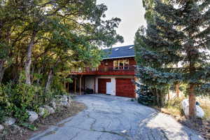 Rustic home with asphalt driveway, an attached garage, a balcony, and roof with shingles