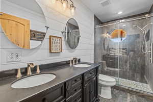 Full bath with a stall shower, double vanity, and wooden walls