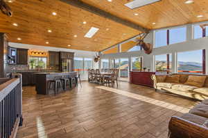 Living room featuring a mountain view, high vaulted ceiling, light wood-style flooring, a wooden ceiling with exposed beams, and a skylight