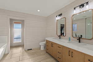 Full bath featuring a bath, recessed lighting, double vanity, wooden walls, and light tile patterned floors