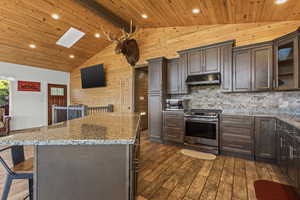 Kitchen featuring dark brown cabinets, a breakfast bar, light stone countertops, stainless steel appliances, and glass insert cabinets
