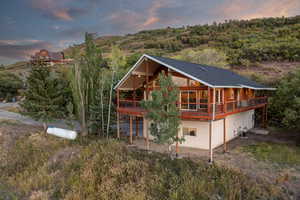 Back of property at dusk featuring a deck, a shingled roof, and a patio