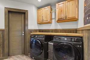 Washroom with cabinet space, washer and clothes dryer, a wainscoted wall, wood finished floors, and wood walls