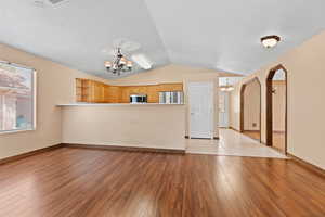Unfurnished living room with a chandelier, light wood-style flooring, arched walkways, and vaulted ceiling
