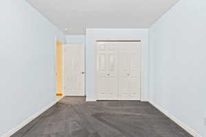 Unfurnished bedroom with dark carpet, a closet, and a textured ceiling