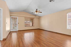Empty room featuring light wood-type flooring, vaulted ceiling, healthy amount of natural light, a ceiling fan, and a textured ceiling