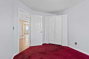 Unfurnished bedroom with dark colored carpet, vaulted ceiling, and a closet