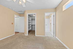 Unfurnished bedroom with light carpet, a walk in closet, attic access, and a ceiling fan