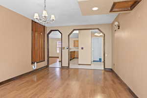 Unfurnished dining area with arched walkways, light wood-style floors, recessed lighting, and a chandelier