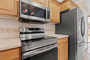 Kitchen featuring stainless steel appliances, backsplash, light brown cabinetry, and light tile patterned floors