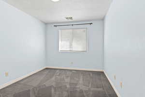 Carpeted empty room with a textured ceiling and baseboards