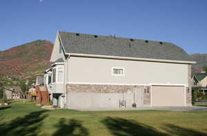 Back of property with a mountain view, stone siding, a lawn, stucco siding, and a garage