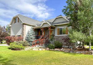 View of front of house featuring stucco siding, stone siding, a front yard, a porch, and roof with shingles