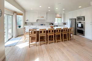 Kitchen with tasteful backsplash, white cabinets, light wood finished floors, stainless steel appliances, and a center island