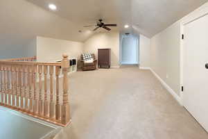 Bonus room featuring a textured ceiling, light carpet, vaulted ceiling, and a ceiling fan