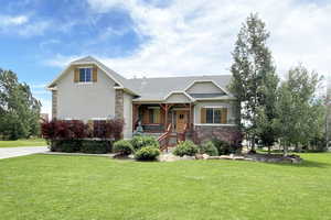 View of front of home with covered porch, stone siding, a front lawn, a shingled roof, and stucco siding