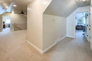 Corridor with a textured ceiling, lofted ceiling, light carpet, and an upstairs landing