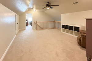 Additional living space featuring a textured ceiling, light colored carpet, lofted ceiling, and ceiling fan