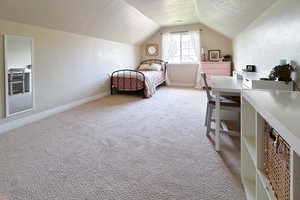 Bedroom with a textured ceiling, light colored carpet, and lofted ceiling