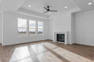 Unfurnished living room featuring a ceiling fan, a glass covered fireplace, recessed lighting, light wood-style flooring, and a raised ceiling