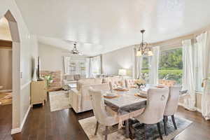 Dining area with dark wood-style flooring, a textured ceiling, ceiling fan, and a chandelier