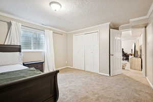 Bedroom with crown molding, light carpet, a textured ceiling, a closet, and a desk