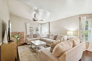 Living room featuring healthy amount of natural light, dark wood-type flooring, a textured ceiling, ceiling fan, and vaulted ceiling