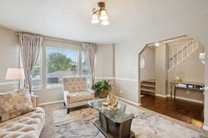 Living area with stairway, arched walkways, wood finished floors, a textured ceiling, and a chandelier