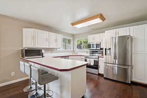 Kitchen with appliances with stainless steel finishes, white cabinetry, a kitchen breakfast bar, dark wood-style flooring, and a textured ceiling