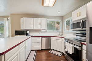 Kitchen featuring appliances with stainless steel finishes, white cabinetry, dark wood-style flooring, light countertops, and a textured ceiling