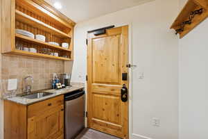 Kitchen with open shelves, light stone counters, stainless steel fridge, tasteful backsplash, and brown cabinetry