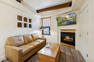 Living area with beam ceiling, a glass covered fireplace, and wood finished floors