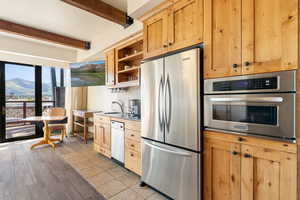Kitchen featuring open shelves, stainless steel appliances, beamed ceiling, a mountain view, and backsplash