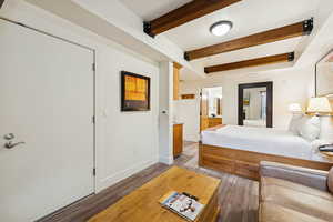 Bedroom with beamed ceiling, light wood-style flooring, and connected bathroom