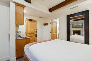 Bedroom featuring beam ceiling, a glass covered fireplace, and recessed lighting