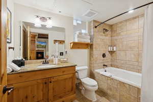 Full bathroom featuring tiled shower / bath, vanity, light tile patterned floors, and a lit fireplace