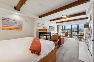 Bedroom with beam ceiling, a multi sided fireplace, freestanding refrigerator, and access to outside