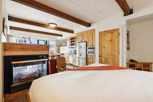 Bedroom featuring beam ceiling, freestanding refrigerator, and a multi sided fireplace