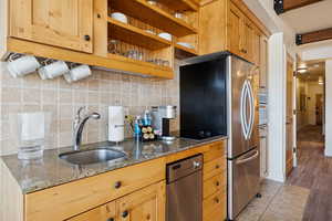 Kitchen featuring dark stone counters, tasteful backsplash, stainless steel appliances, and light brown cabinetry
